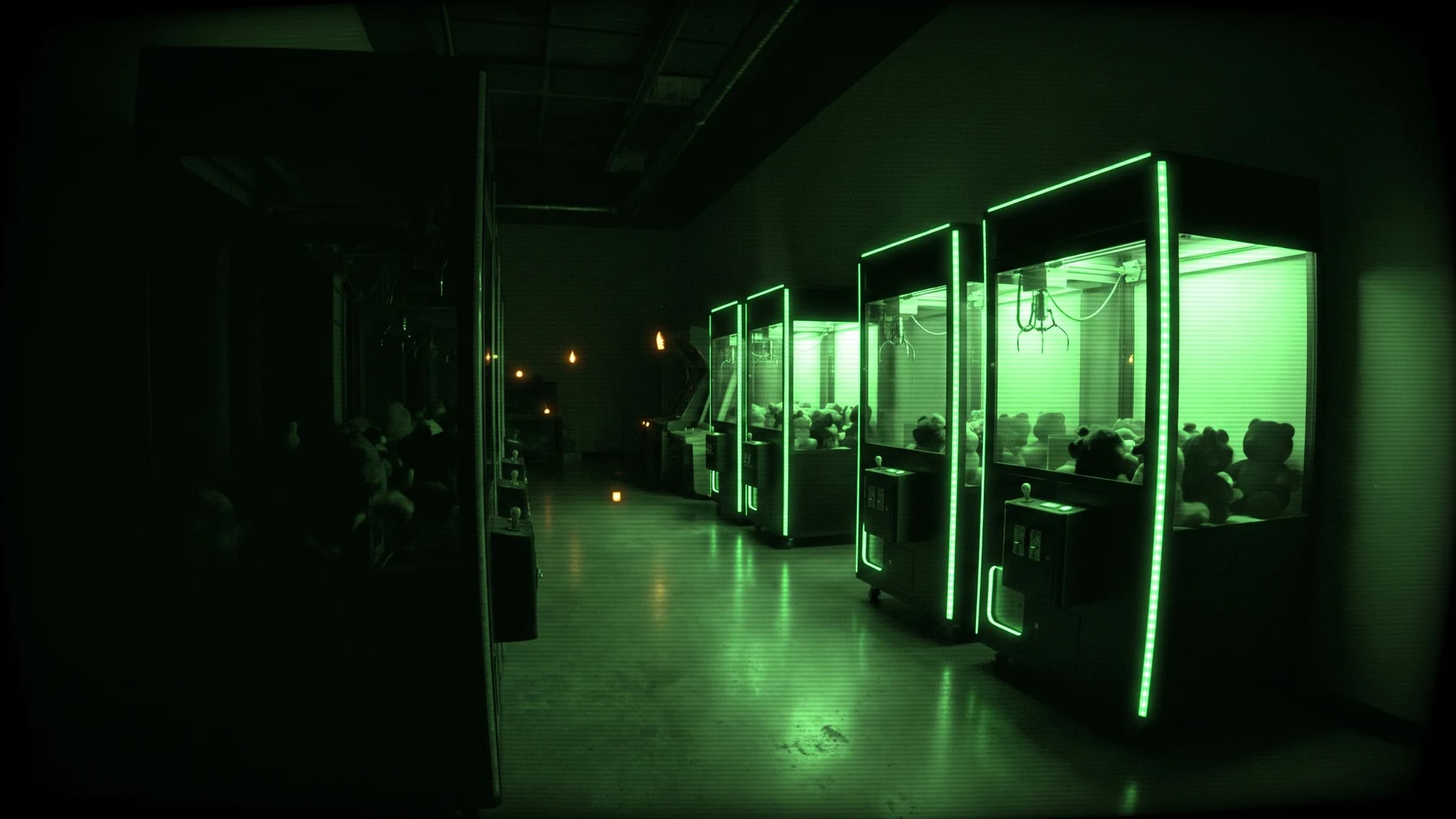 Night-vision view down a dark arcade aisle lined with glowing claw machines